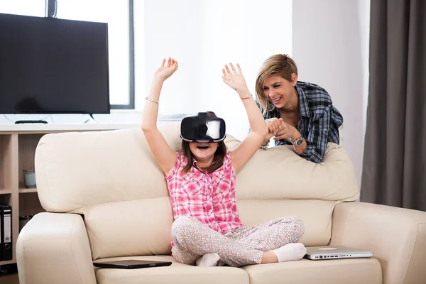 Mother in the living room sitting next to her daughter that is wearing a virtual reality headset