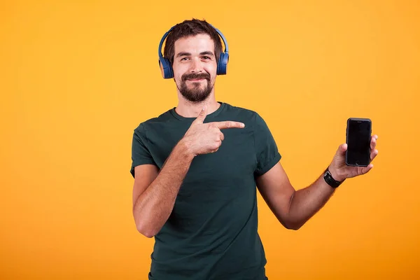 Fröhlicher, fröhlicher Mann mit Kopfhörern, der auf sein Smartphone zeigt — Stockfoto