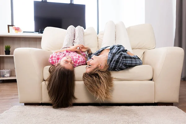 Beautiful mother with her cute daughter lying on the couch with their head upside down