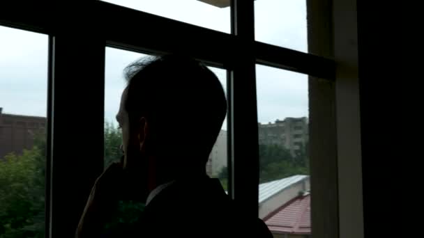 Hombre de negocios en silueta mirando por la ventana de su oficina — Vídeos de Stock