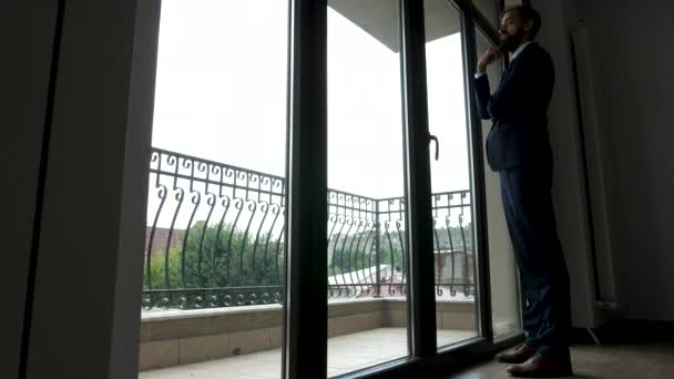 El hombre de negocios de cuerpo completo se para frente a grandes ventanas en su oficina — Vídeos de Stock