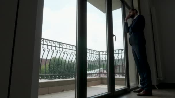 Silueta de cuerpo completo de un hombre de negocios se para y mira fuera de las ventanas de insectos en su oficina — Vídeo de stock