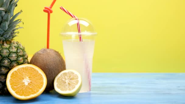 Coco, laranja fatiada e limão e um abacaxi ao lado de uma xícara de plástico com suco fresco — Vídeo de Stock