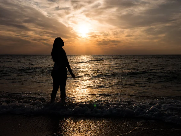 Silhouette di una giovane ragazza sulla spiaggia. giovane ragazza cammina al tramonto in riva al mare . — Foto Stock