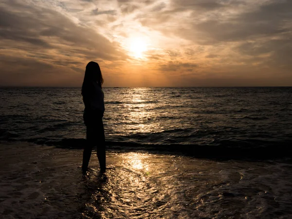 Silhouette di una giovane ragazza sulla spiaggia. giovane ragazza cammina al tramonto in riva al mare . — Foto Stock