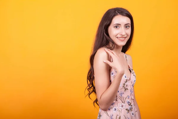 Aantrekkelijke jonge vrouw smilling op de camera in de studio over de gele achtergrond in korte jurk — Stockfoto