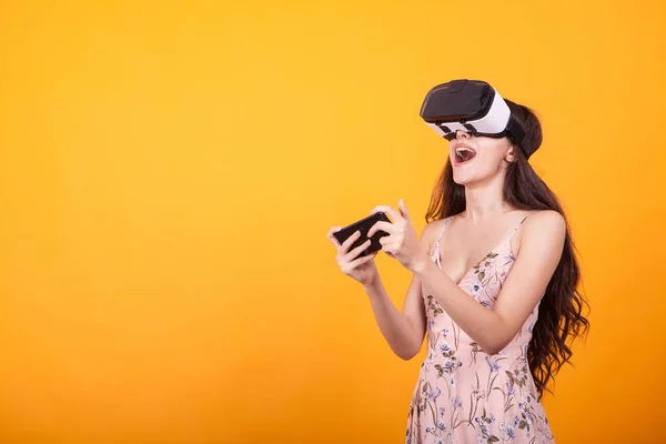 Woman wearing a futuristic looking virtual reality headset goggles in studio over yellow background
