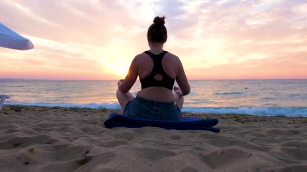 Γυναίκα κάθεται στην παραλία εξάσκηση γιόγκα στο sunrise — Αρχείο Βίντεο