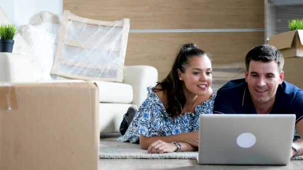 Feliz casal sorrindo deitado no chão escolhendo novos móveis online — Vídeo de Stock