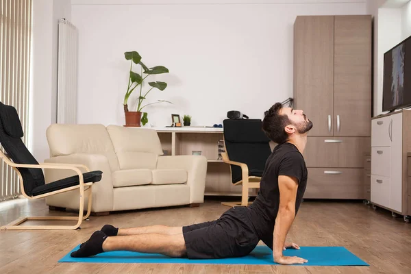 Young adult doing cobra yoga pose on his house floor — Stock Photo, Image