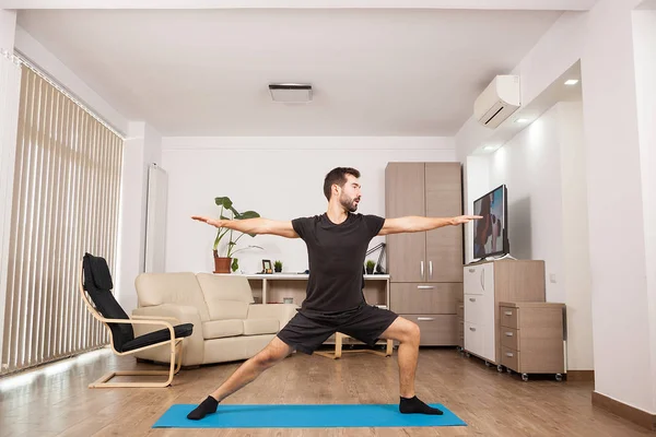 Bebaarde man doen Warrior Ii yoga poseren en zijn spieren uit te rekken — Stockfoto
