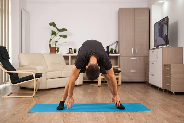 Staande voorwaartse yoga pose gemaakt door pasvorm volwassen op de vloer van zijn huis — Stockfoto