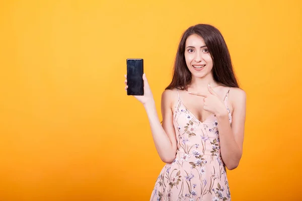 Linda mujer joven señalando en su teléfono en el estudio sobre fondo amarillo — Foto de Stock