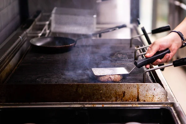 Chef está grelhando um hambúrguer de carne na grelha — Fotografia de Stock