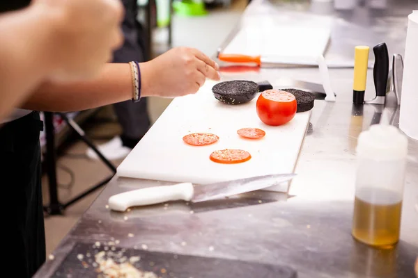 Koch schneidet Tomaten für Burger in Küche — Stockfoto