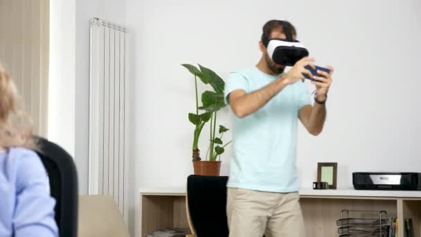 Homme joue à des jeux de réalité virtuelle dans le salon tandis que sa petite amie essaie de travailler sur l'ordinateur — Video