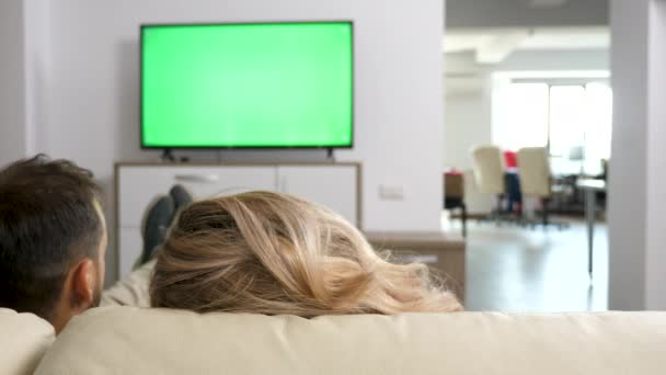 Мужчина и женщина уютно на диване смотрят телевизор с зеленым экраном — стоковое видео