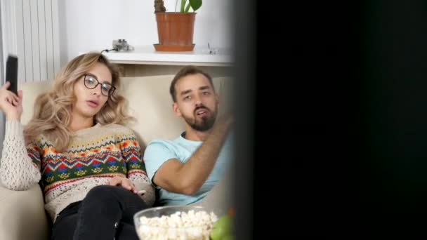 Tanulságos lövés pár pattogatott kukoricát eszik, és tévénézés a nappali — Stock videók
