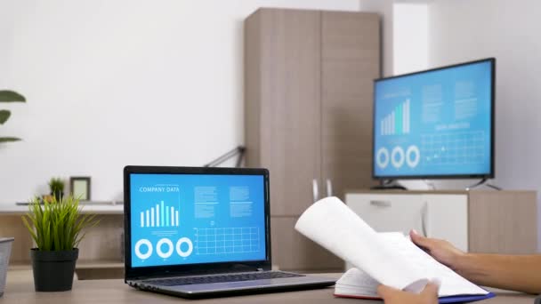 Mand, der arbejder ved skrivebordet i stuen kontrollere nogle data på computerskærmen – Stock-video