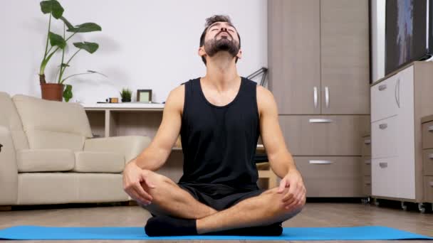 Fit young man sits on a blue mat on the floor of his house and stretches — Stock Video