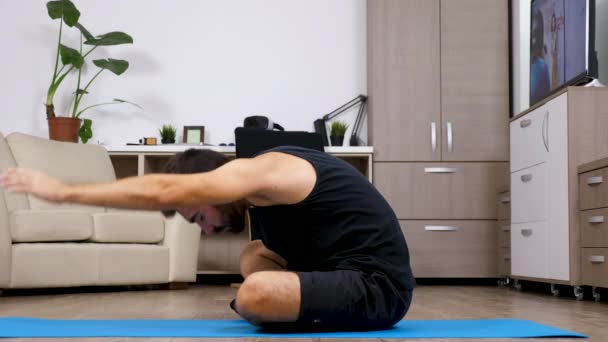 Hombre haciendo diferentes posturas de yoga en una alfombra azul en su casa — Vídeo de stock