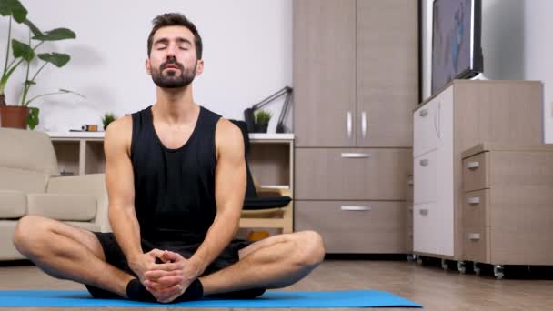 Young passen man doen yoga, de lotus pose, op de verdieping van zijn woning — Stockvideo