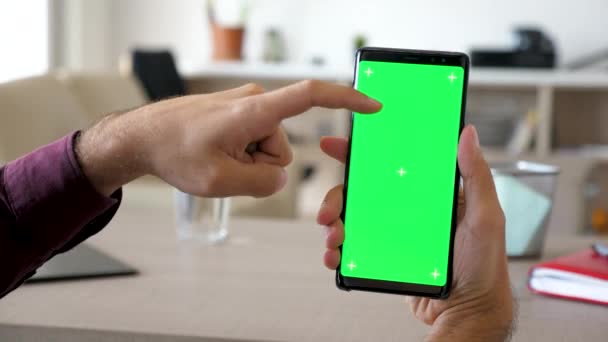 Homem usando um smartphone moderno com tela verde chroma mock-up em sua sala de estar — Vídeo de Stock