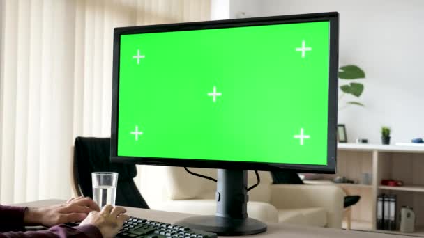 Неузнаваемый человек, печатающий на клавиатуре персонального компьютера с большим зеленым экраном — стоковое видео