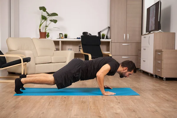 Bebaarde man doet push ups op de vloer van zijn huis. — Stockfoto