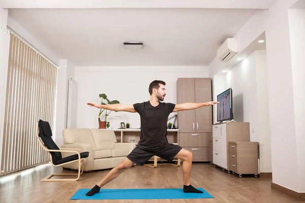 Bebaarde man doen Warrior Ii yoga poseren en zijn spieren uit te rekken — Stockfoto