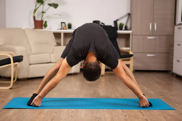 Staande voorwaartse yoga pose gemaakt door pasvorm volwassen op de vloer van zijn huis — Stockfoto