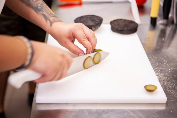 Chef schneidet Essiggurken für leckeren Burger im Restaurant — Stockfoto