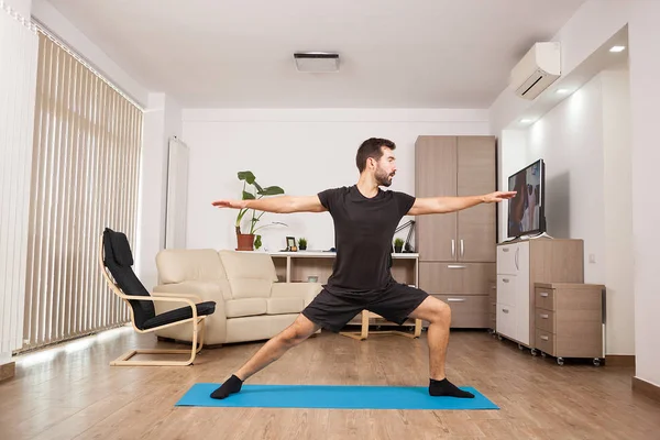 Bebaarde man doen Warrior Ii yoga poseren en zijn spieren uit te rekken — Stockfoto