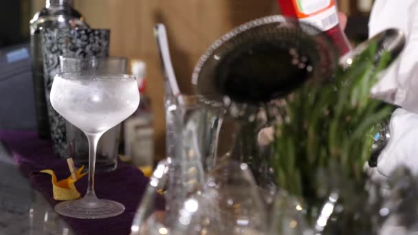 Gefrorenes Glas vor dem Rahmen mit einem Barkeeper, der einen Cocktail zubereitet — Stockvideo