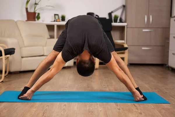 Staande voorwaartse yoga pose gemaakt door pasvorm volwassen op de vloer van zijn huis — Stockfoto