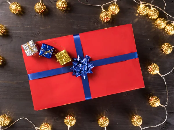 Красная подарочная коробка с маленькими подарочными коробками на темном деревянном полу в окружении золотых огней — стоковое фото