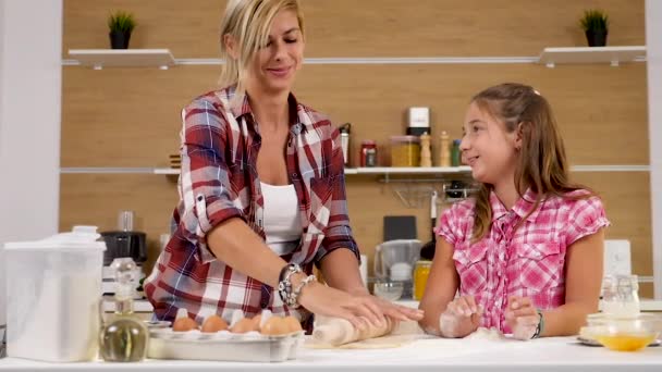 Young daughter throws flour in the air while her mother knead dough next to her — Stock Video