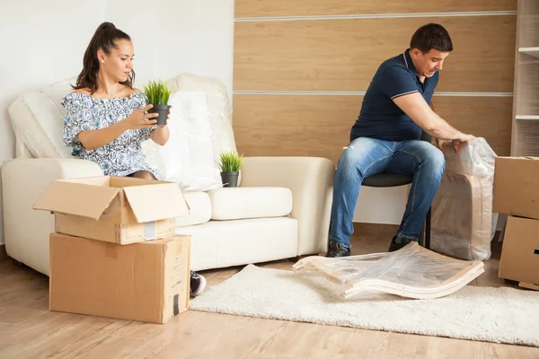 Молодая улыбающаяся пара распаковывает картонные коробки вместе, сидя на диване . — стоковое фото