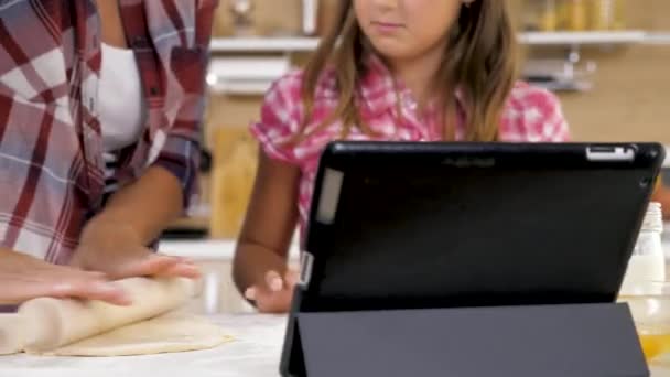 Madre e hija cocinando en la cocina y mirando una tableta digital para la receta — Vídeos de Stock