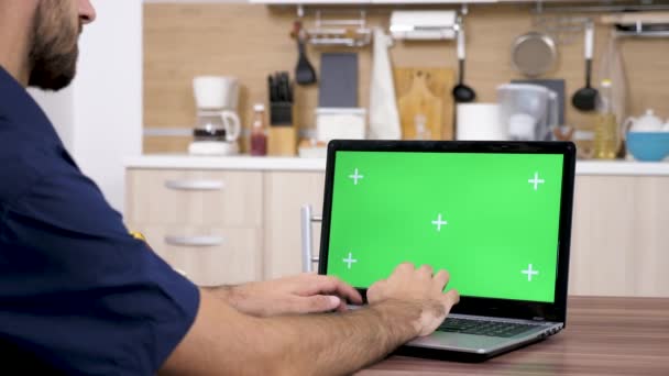 Человек на кухне печатает на клавиатуре ноутбука с зеленым экраном — стоковое видео
