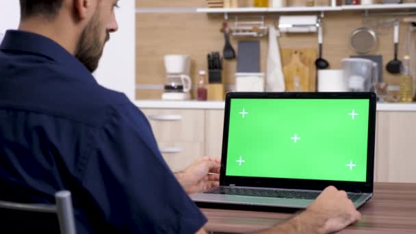 Человек на кухне смотрит на компьютер с зеленым экраном макет — стоковое видео