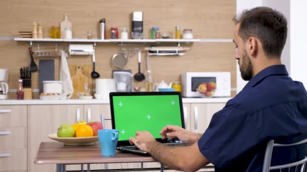 Joven en la cocina escribiendo en el teclado de la computadora — Vídeo de stock