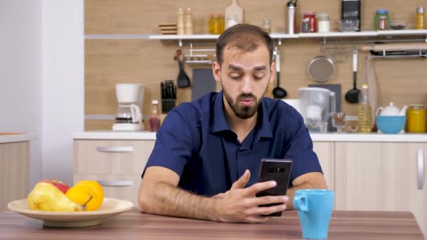 Um homem na cozinha a falar com alguém ao telefone — Vídeo de Stock