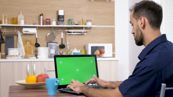 Homem na mesa na cozinha bebendo café e digitando no computador — Vídeo de Stock