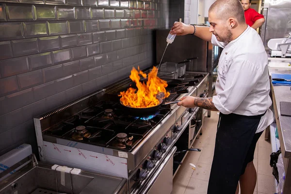 Cozinheiro masculino fazendo marisco inflamatório no fogão na cozinha do restaurante — Fotografia de Stock