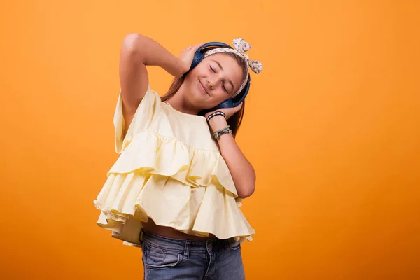 Menina feliz ouvir música em seus fones de ouvido em estúdio no fundo amarelo — Fotografia de Stock