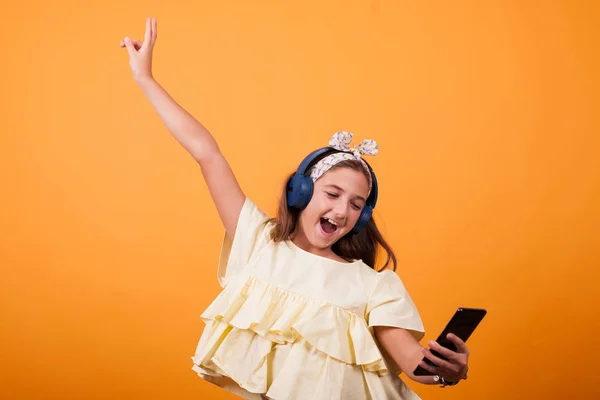 Menina feliz ouvir música em seus fones de ouvido em estúdio no fundo amarelo — Fotografia de Stock