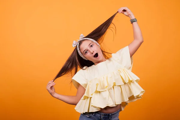 Menina brincando com o cabelo em uma sessão de fotos em estúdio no fundo amarelo — Fotografia de Stock