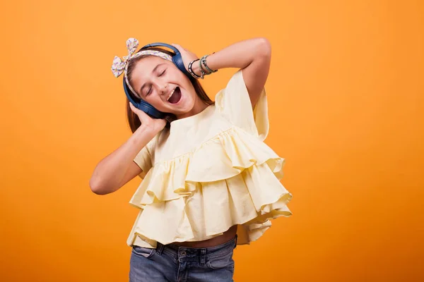 Щаслива дівчина слухає музику на своїх навушниках в студії на жовтому фоні — стокове фото
