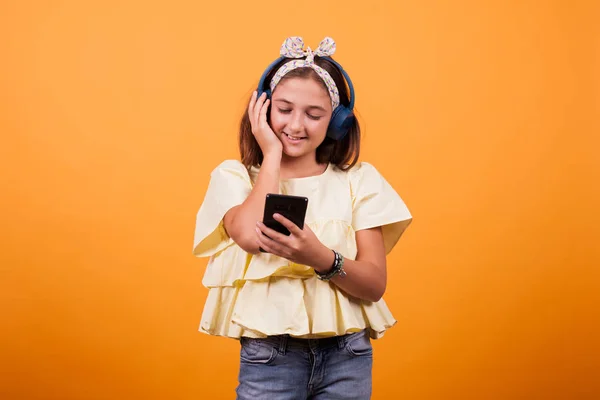 Счастливая девушка слушает музыку в наушниках в студии на желтом фоне — стоковое фото